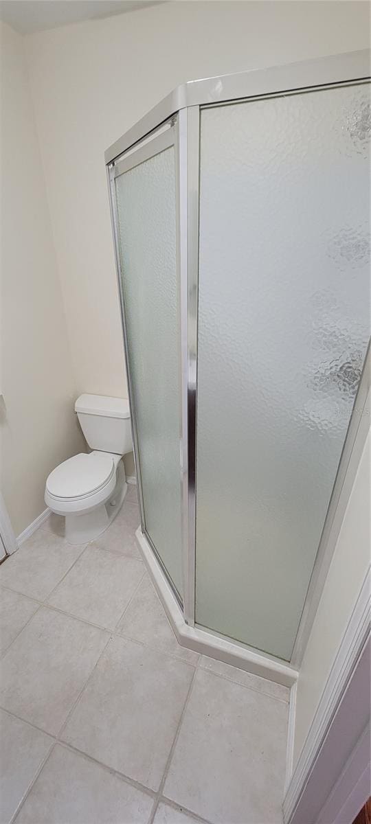 bathroom featuring a stall shower, baseboards, toilet, and tile patterned floors