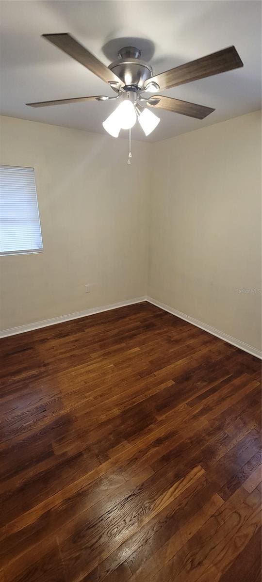 empty room featuring dark wood finished floors, a ceiling fan, and baseboards