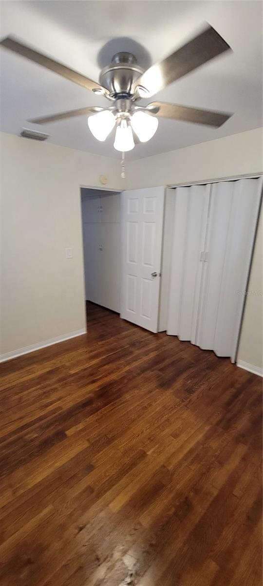 unfurnished bedroom featuring dark wood-style floors, ceiling fan, visible vents, and baseboards