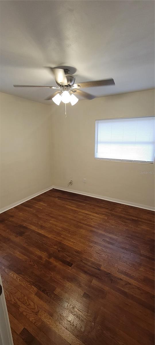 unfurnished room with dark wood-type flooring, ceiling fan, and baseboards