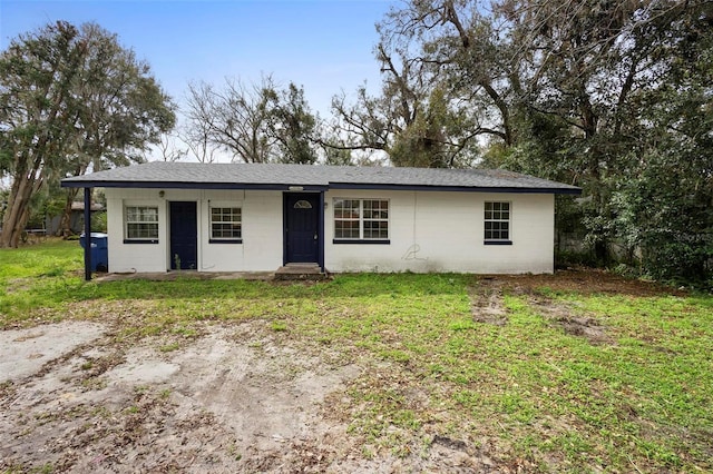 ranch-style home with a shingled roof, concrete block siding, and a front lawn