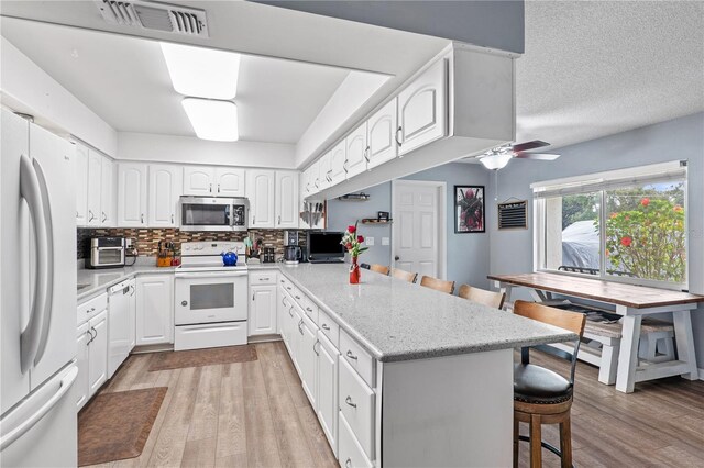 445 Virginia Ave, Saint Cloud, FL 34769 - kitchen with white appliances, a kitchen bar, a peninsula, light wood-style flooring, and white cabinetry