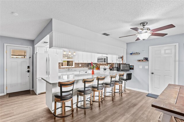 445 Virginia Ave, Saint Cloud, FL 34769 - kitchen with white appliances, a sink, light wood finished floors, a textured ceiling, and a breakfast bar