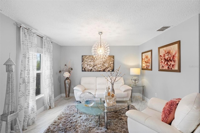 living area featuring a textured ceiling, baseboards, visible vents, and a notable chandelier