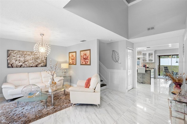 living area featuring visible vents, a wainscoted wall, marble finish floor, a textured ceiling, and a decorative wall