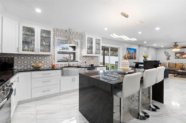 kitchen with appliances with stainless steel finishes, glass insert cabinets, hanging light fixtures, white cabinetry, and a sink