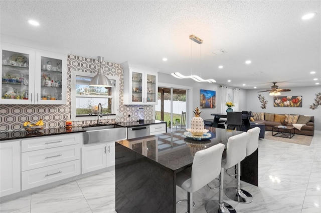 kitchen with pendant lighting, stainless steel dishwasher, glass insert cabinets, white cabinets, and a sink