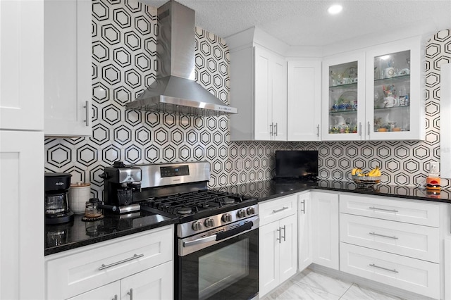 kitchen with marble finish floor, glass insert cabinets, white cabinetry, wall chimney range hood, and gas range