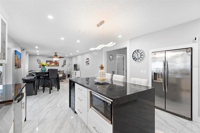 kitchen with a center island, pendant lighting, stainless steel appliances, white cabinetry, and dark stone counters