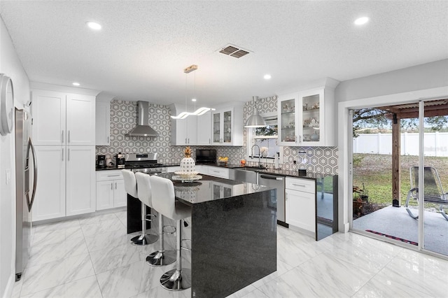 kitchen featuring stainless steel appliances, a kitchen island, visible vents, wall chimney exhaust hood, and pendant lighting