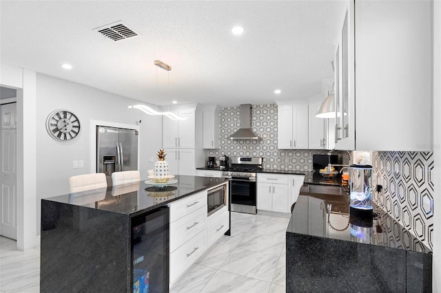 kitchen featuring a center island, stainless steel appliances, white cabinets, wall chimney range hood, and dark stone counters