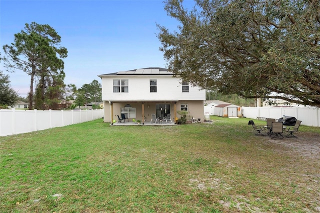 back of house with a fenced backyard, an outbuilding, a storage unit, a patio area, and roof mounted solar panels