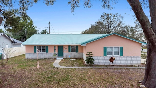 single story home featuring stucco siding, metal roof, fence, a front lawn, and brick siding