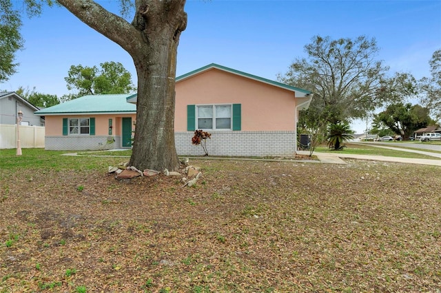 ranch-style house with stucco siding, fence, a front lawn, and brick siding