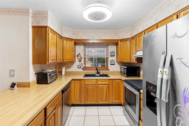 kitchen with under cabinet range hood, a sink, light countertops, appliances with stainless steel finishes, and wallpapered walls