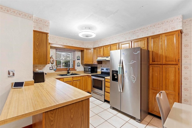 kitchen with wallpapered walls, stainless steel appliances, light countertops, under cabinet range hood, and a sink