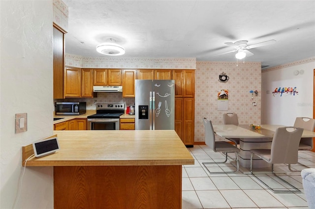 kitchen with light tile patterned floors, under cabinet range hood, a peninsula, light countertops, and appliances with stainless steel finishes