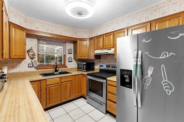 kitchen with under cabinet range hood, stainless steel appliances, butcher block countertops, a sink, and wallpapered walls