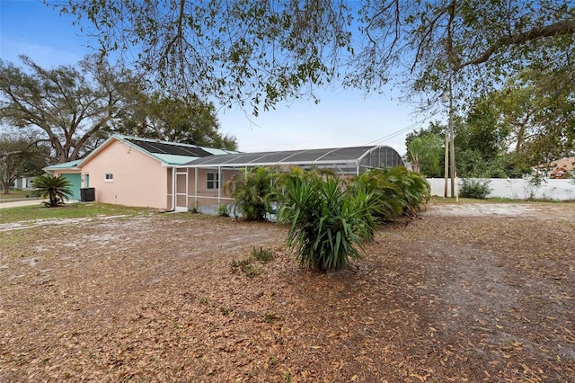 rear view of property featuring metal roof, a lanai, central air condition unit, fence, and stucco siding