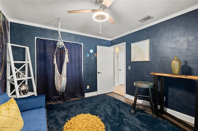 interior space featuring crown molding, visible vents, a textured wall, a ceiling fan, and a textured ceiling