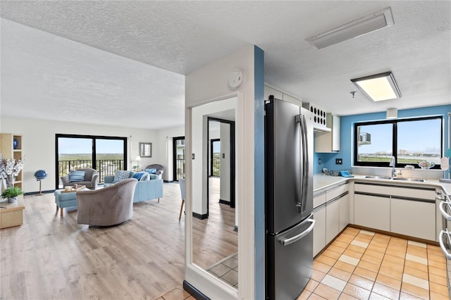 kitchen with open floor plan, freestanding refrigerator, light countertops, white cabinetry, and a sink