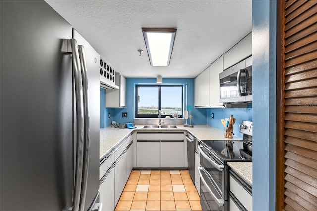 kitchen featuring light tile patterned floors, stainless steel appliances, light countertops, white cabinets, and a sink