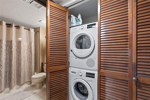 laundry area with visible vents, a textured ceiling, stacked washing maching and dryer, laundry area, and tile patterned floors