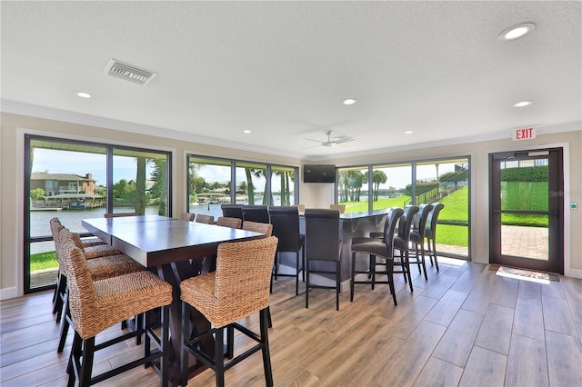 dining space featuring visible vents, wood finished floors, a water view, crown molding, and recessed lighting