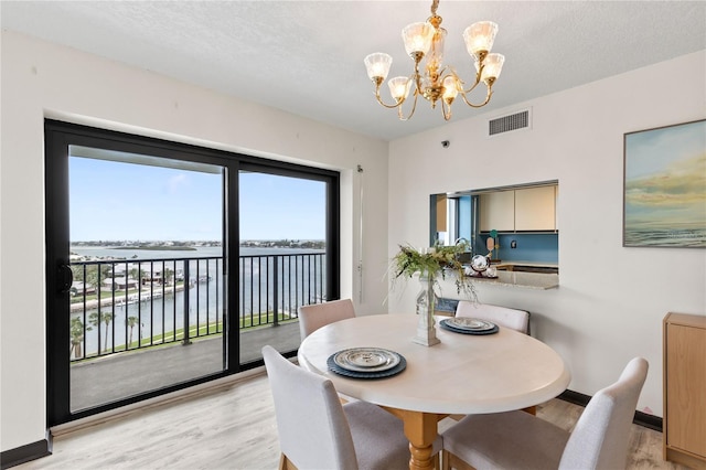 dining space featuring a water view, visible vents, light wood-style floors, a chandelier, and baseboards