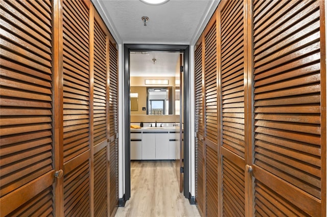 corridor with light wood-style floors, a textured ceiling, and a sink