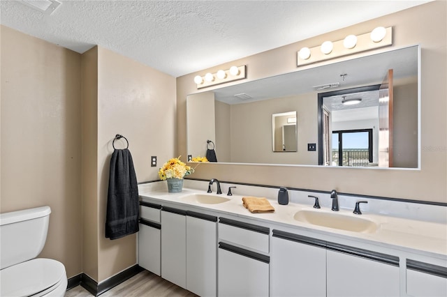 bathroom with a textured ceiling, double vanity, a sink, and toilet