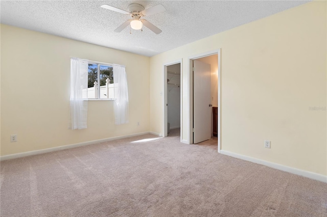 unfurnished bedroom with a textured ceiling, baseboards, a spacious closet, and light colored carpet
