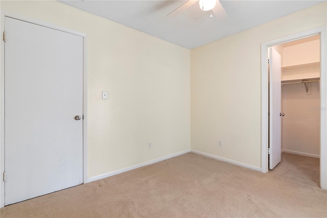 unfurnished bedroom featuring baseboards, light colored carpet, a ceiling fan, a closet, and a walk in closet