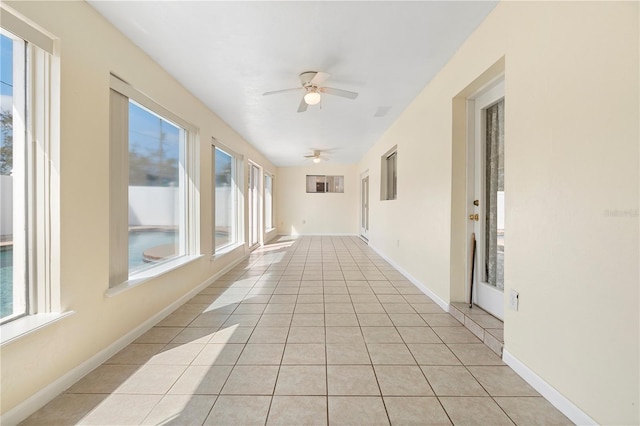hallway featuring baseboards, a healthy amount of sunlight, and light tile patterned floors