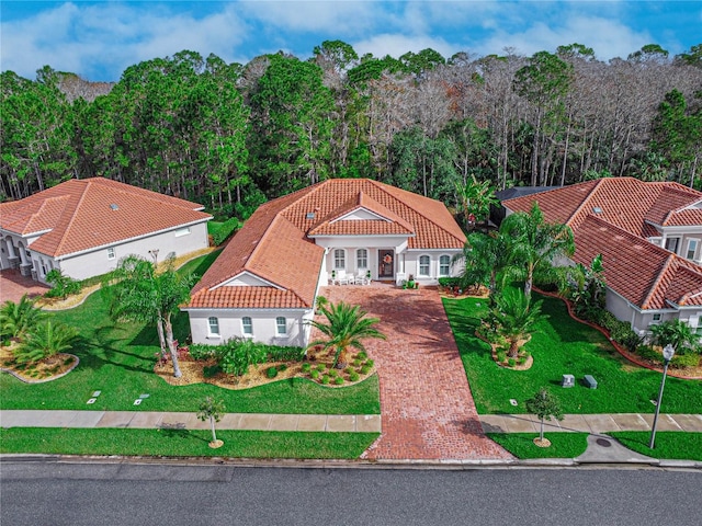 view of front of house with decorative driveway, a tile roof, and a view of trees