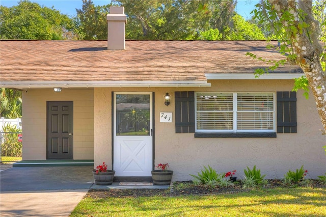 view of front of house featuring a front yard, stucco siding, a chimney, and roof with shingles