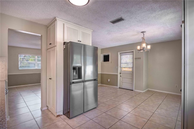 kitchen with light tile patterned floors, stainless steel fridge, baseboards, white cabinets, and a chandelier