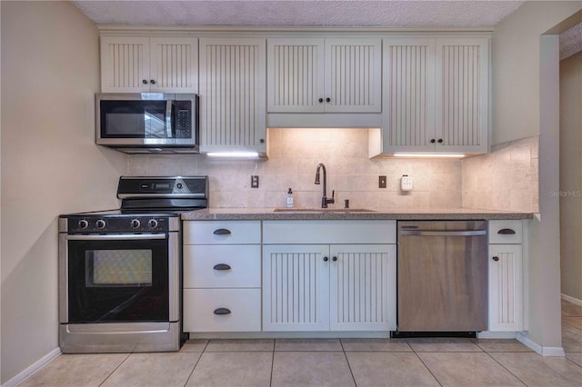 kitchen featuring appliances with stainless steel finishes, a sink, backsplash, and light tile patterned floors