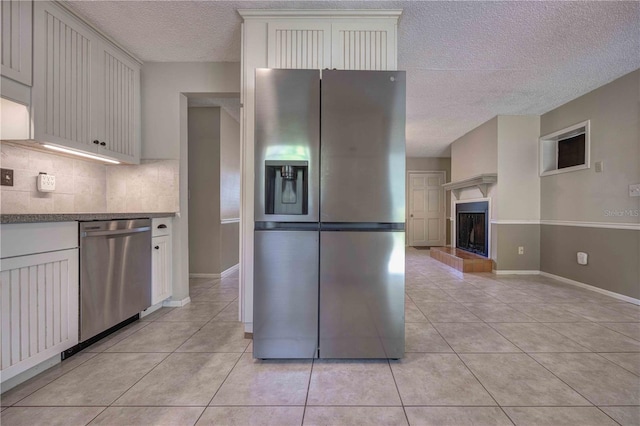 kitchen featuring stainless steel appliances, tasteful backsplash, a fireplace with raised hearth, light tile patterned flooring, and white cabinetry