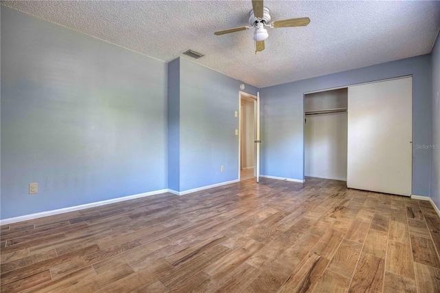 unfurnished bedroom featuring a closet, visible vents, a textured ceiling, wood finished floors, and baseboards