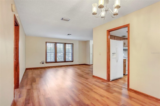 unfurnished room featuring a textured ceiling, light wood-style flooring, visible vents, baseboards, and an inviting chandelier