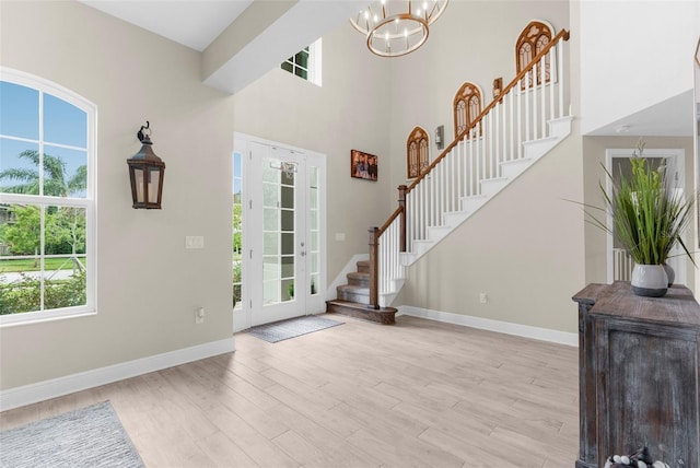 foyer with a towering ceiling, baseboards, stairs, light wood-type flooring, and an inviting chandelier