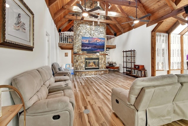 living area with wooden ceiling, light wood-style floors, a ceiling fan, and a stone fireplace