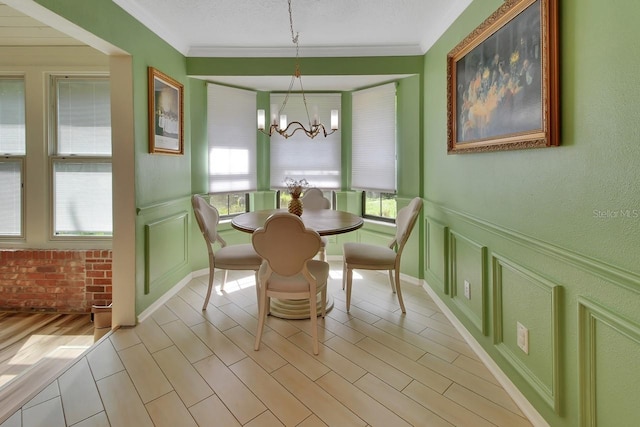 dining area with crown molding, light wood-type flooring, a decorative wall, and an inviting chandelier