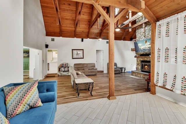 living area featuring a stone fireplace, wood finished floors, high vaulted ceiling, wooden ceiling, and beamed ceiling