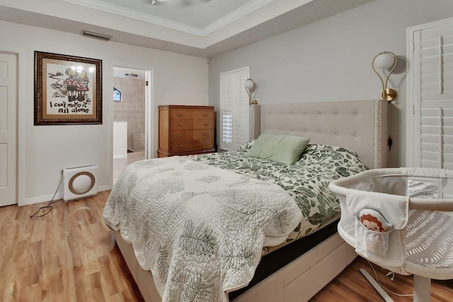 bedroom with wood finished floors, visible vents, baseboards, a raised ceiling, and crown molding