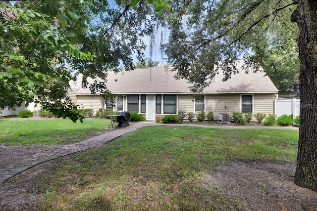 ranch-style house featuring a front lawn, a shingled roof, and fence