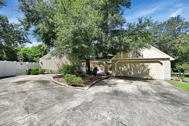 view of property hidden behind natural elements with fence, driveway, and a garage