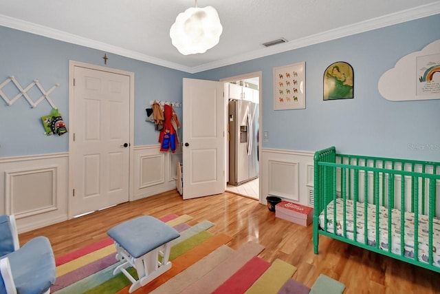 bedroom featuring visible vents, ornamental molding, stainless steel fridge, a wainscoted wall, and light wood-style flooring