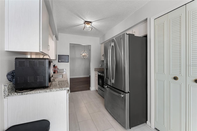 kitchen featuring baseboards, white cabinets, appliances with stainless steel finishes, an inviting chandelier, and a textured ceiling